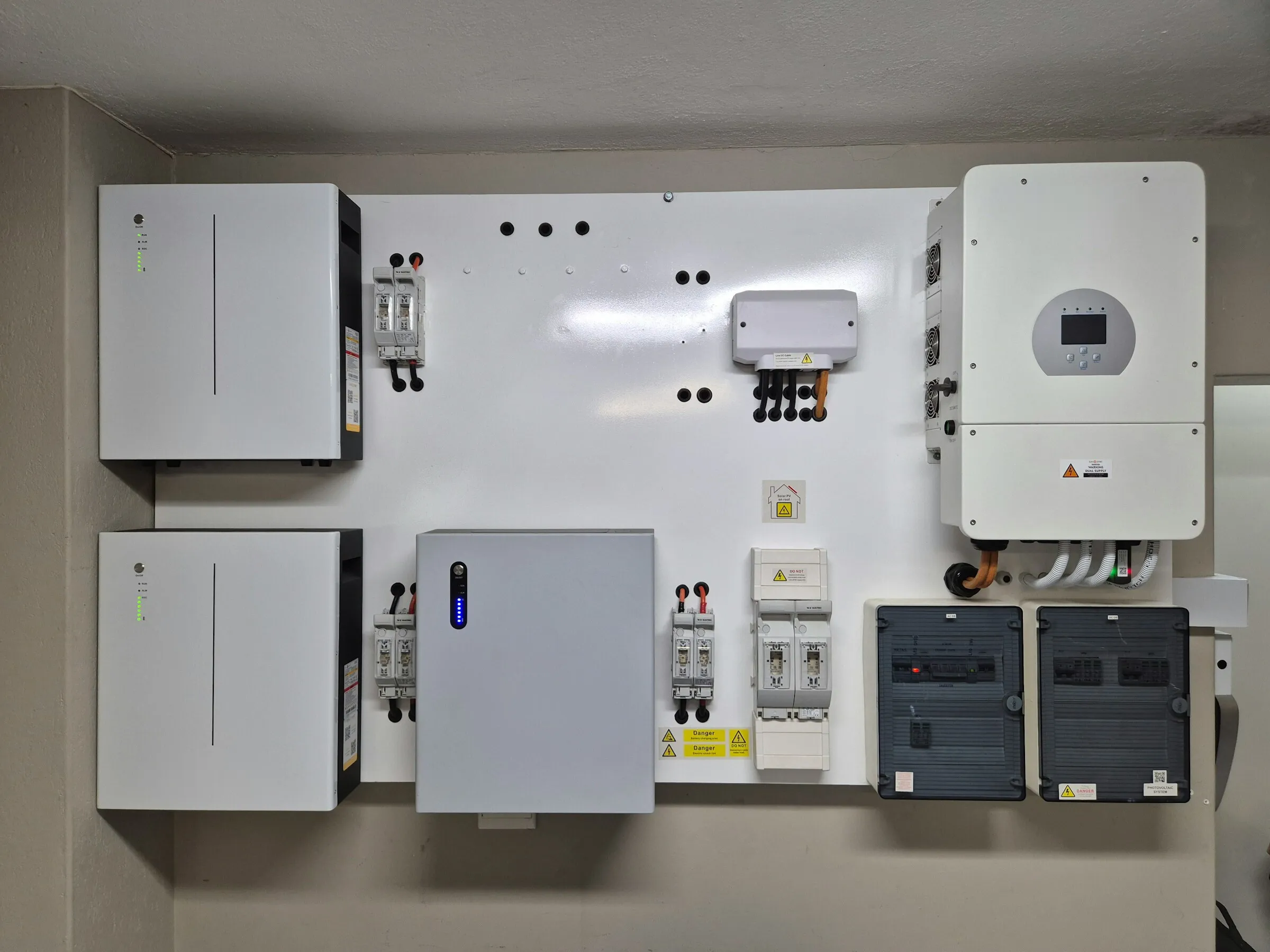 Wall-mounted lithium battery units next to a hybrid inverter and breaker panels