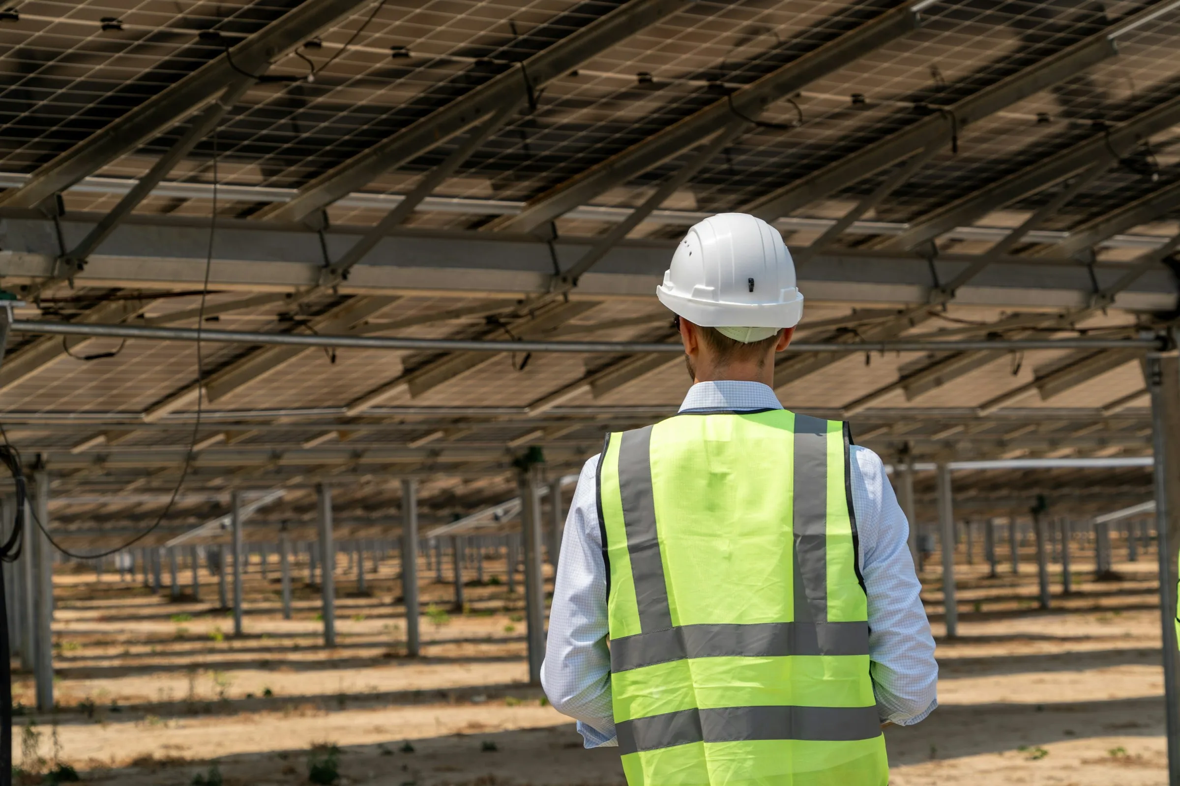 Engineer in a hard hat and safety vest checking rows of solar panels